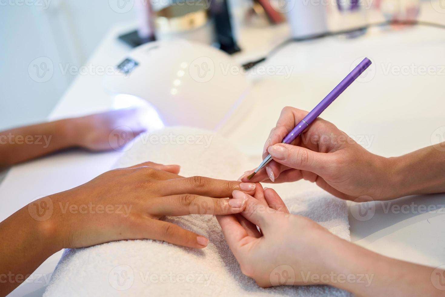 close-up van schoonheidsspecialiste die de nagels van een vrouw schildert met een borstel in een nagelsalon foto