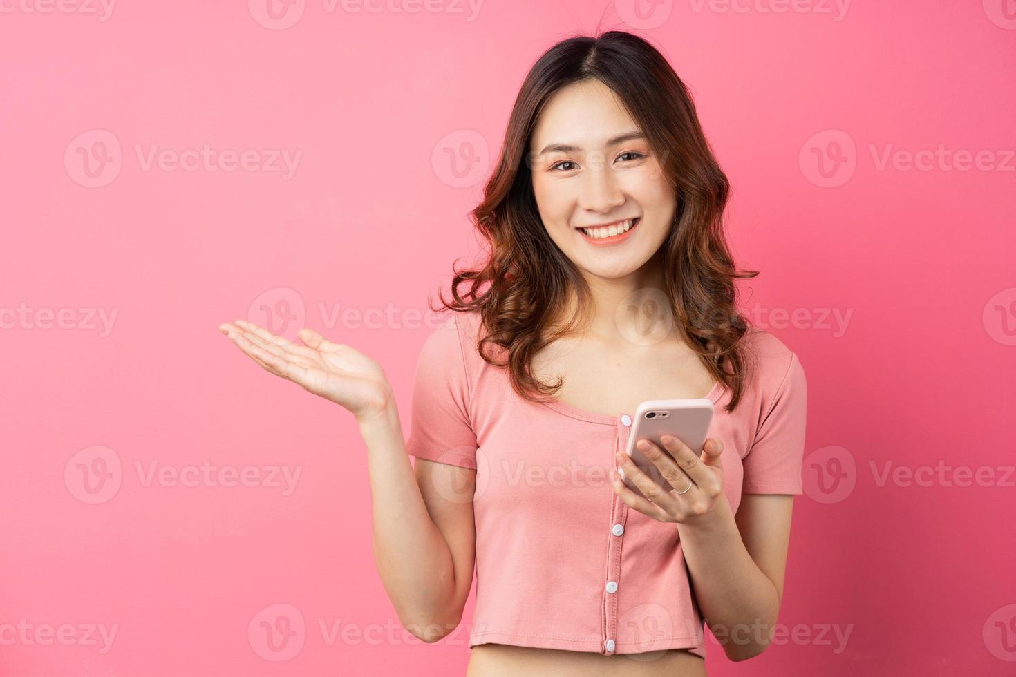 jonge aziatische vrouw die de telefoon op roze achtergrond gebruikt foto