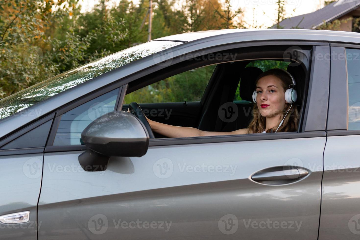 een jonge, mooie vrouw met lang haar en koptelefoon zit aan het stuur van de auto. foto