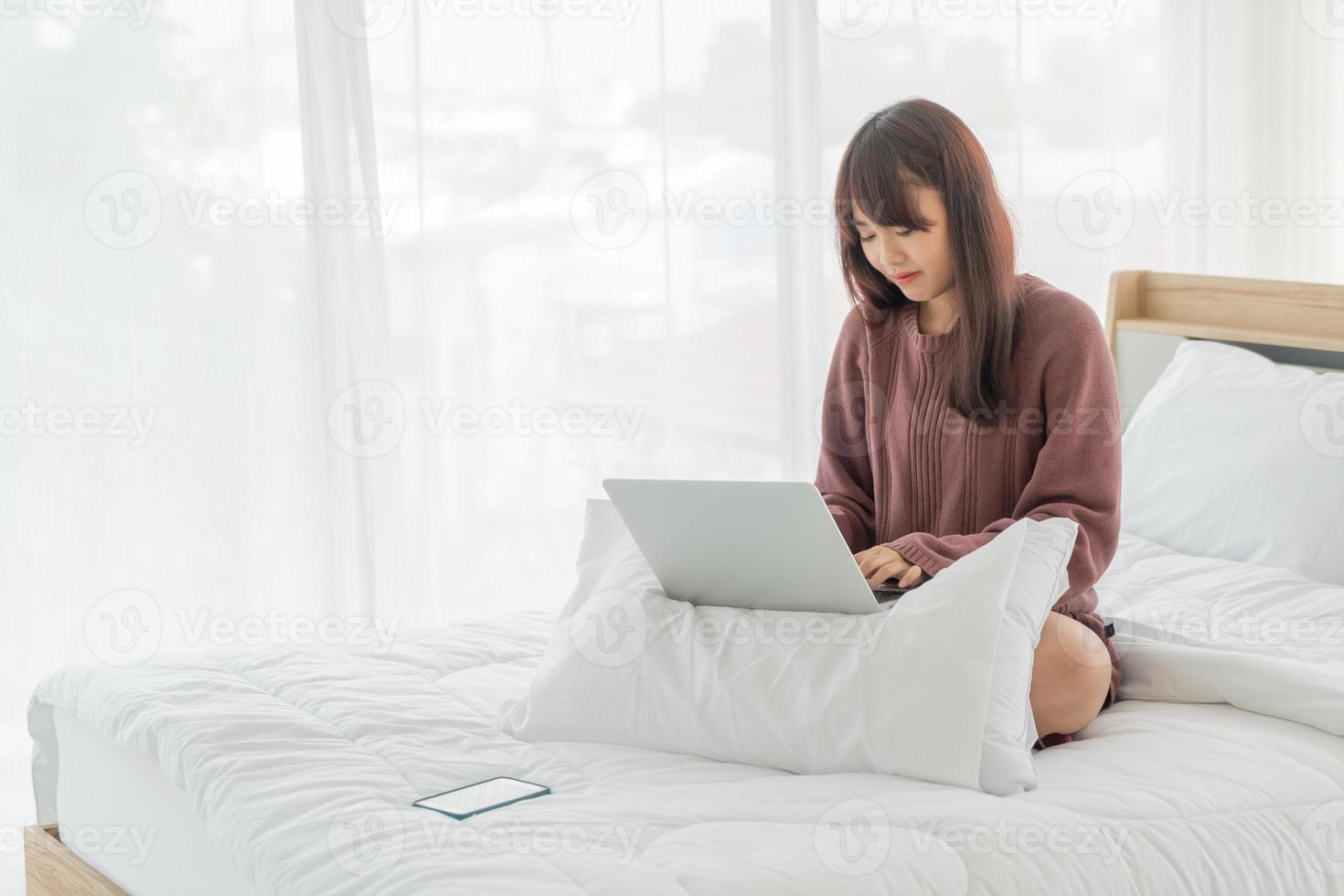 Aziatische vrouw die met laptop op bed thuis werkt at foto