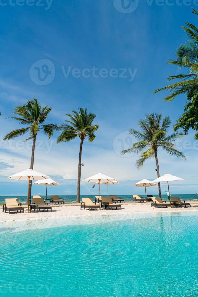 stoelzwembaden of bedden en parasols rond het zwembad met zeeachtergrond - vakantie en vakantieconcept foto