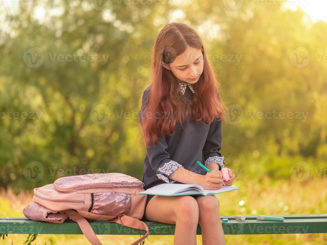 meisje tiener schoolmeisje schrijft in een notitieblok zittend op een bankje. foto