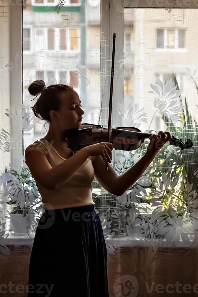 silhouet van een jong meisje, een muzikant. viool spelen op de achtergrond van het raam foto