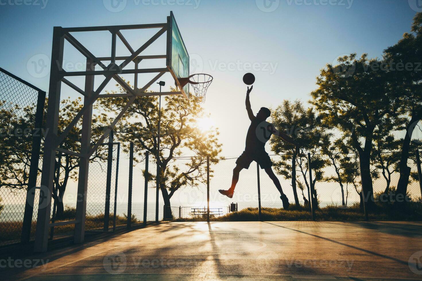 zwart Mens aan het doen sport, spelen basketbal Aan zonsopkomst, jumping silhouet foto