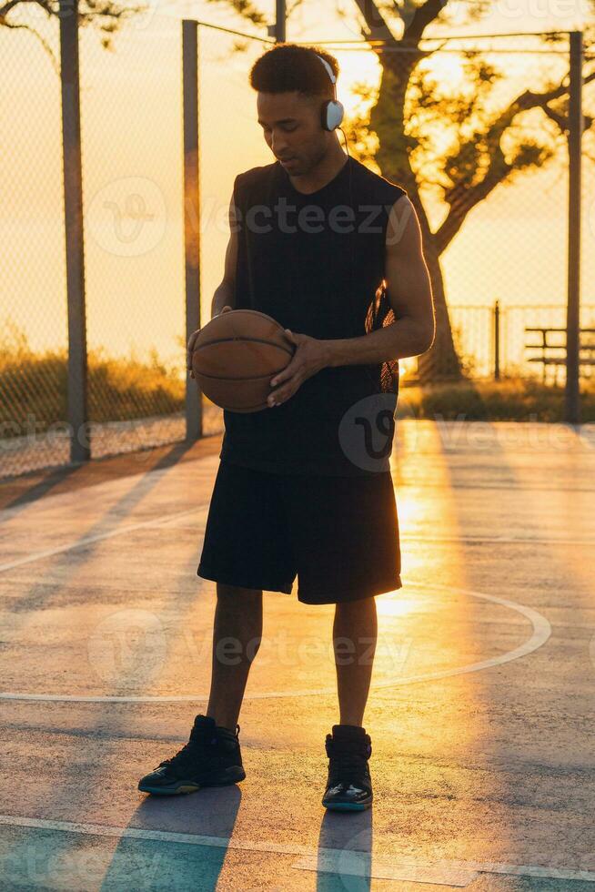 zwart Mens aan het doen sport, spelen basketbal Aan zonsopkomst, actief levensstijl, zonnig zomer ochtend- foto