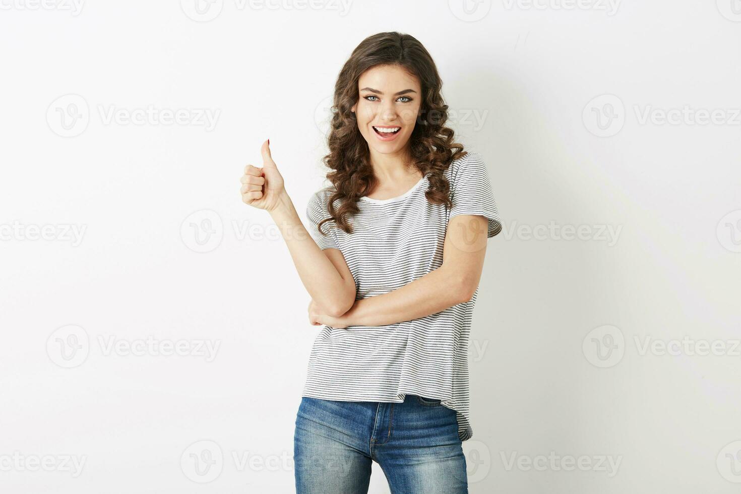 jong aantrekkelijk vrouw gekleed in gewoontjes kleding t-shirt en jeans tonen positief gebaar, lachend, Vrolijk, hipster stijl, geïsoleerd, krullend, duim omhoog foto