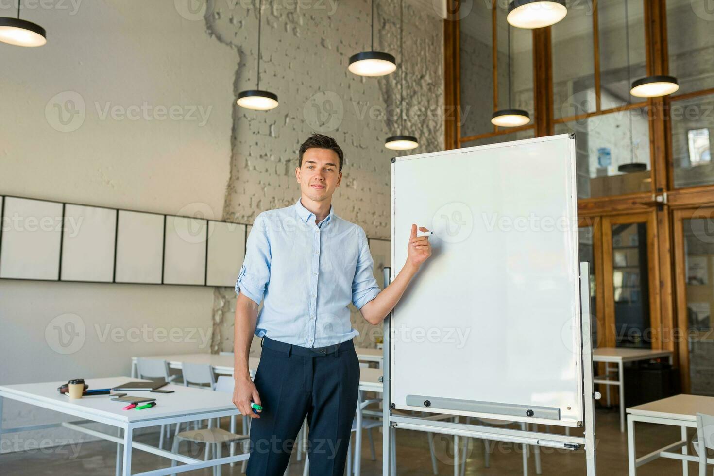 zelfverzekerd jong knap glimlachen Mens staand Bij leeg wit bord met markeerstift foto