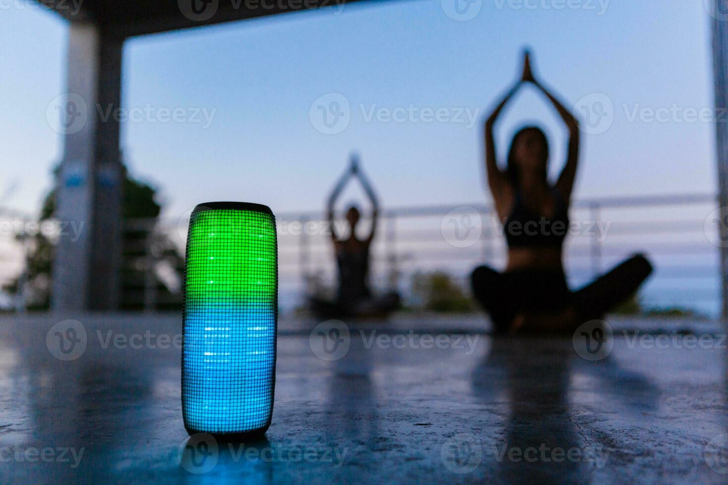 draadloze spreker Aan voorgrond van bedrijf van vrienden aan het doen yoga luisteren naar muziek- in schemer foto