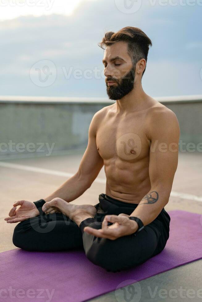 aantrekkelijk knap Mens met atletisch sterk lichaam aan het doen ochtend- yoga dzen meditatie foto