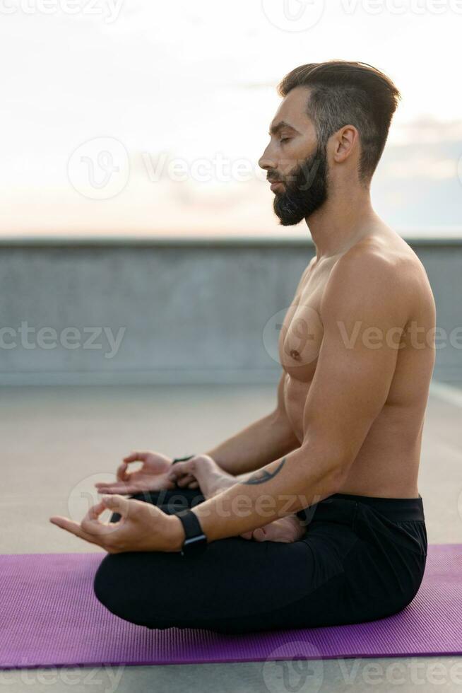 aantrekkelijk knap Mens met atletisch sterk lichaam aan het doen ochtend- yoga dzen meditatie foto