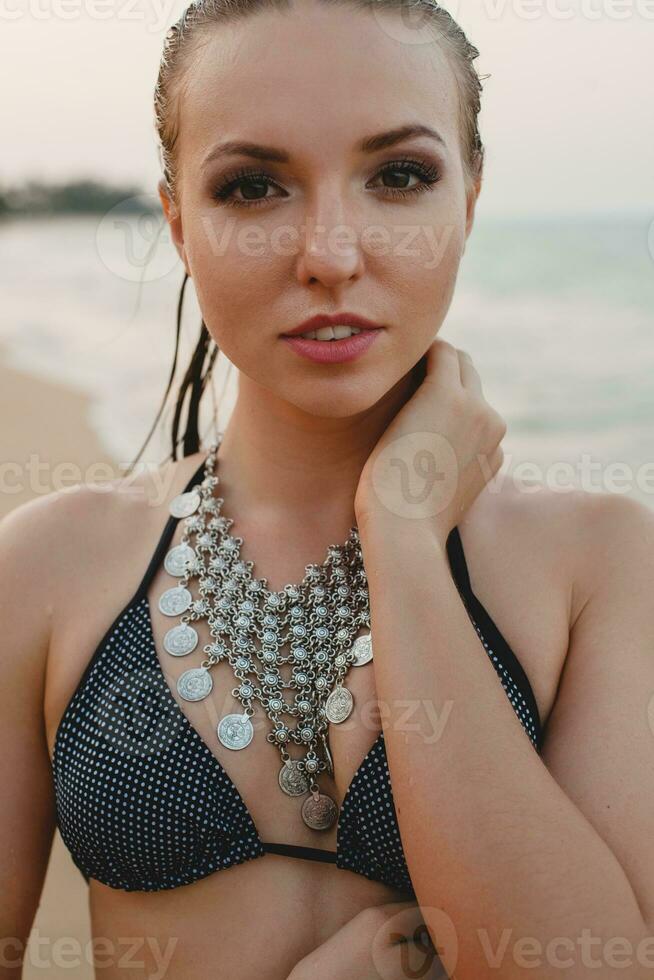 jong mooi blond vrouw zonnen Aan zand strand in bikini zwemmen pak, wijnoogst ketting foto
