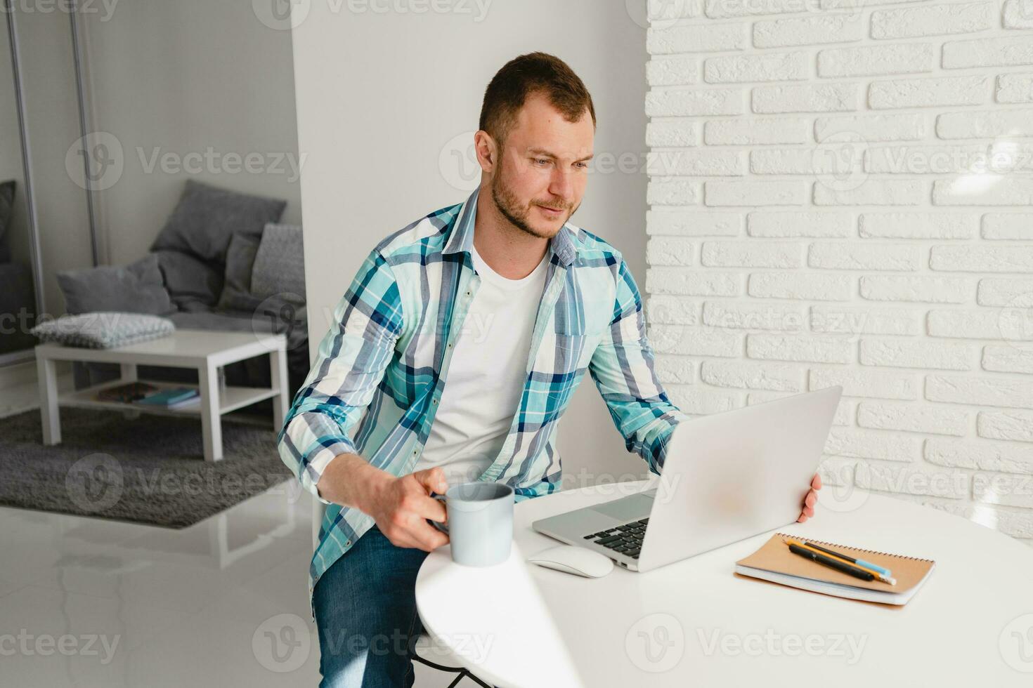 knap glimlachen Mens in overhemd zittend in keuken Bij huis Bij tafel werken online Aan laptop foto