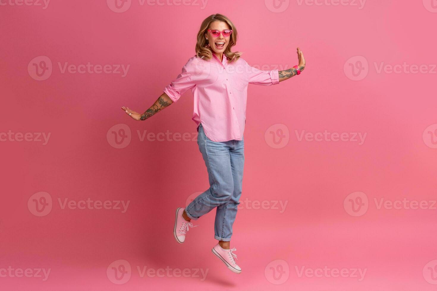 blond mooi vrouw in roze overhemd en jeans glimlachen jumping foto
