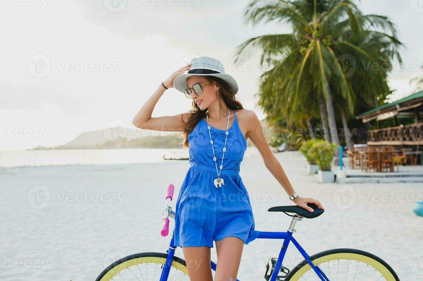 jong aantrekkelijk glimlachen vrouw in blauw jurk wandelen Aan tropisch strand met fiets foto