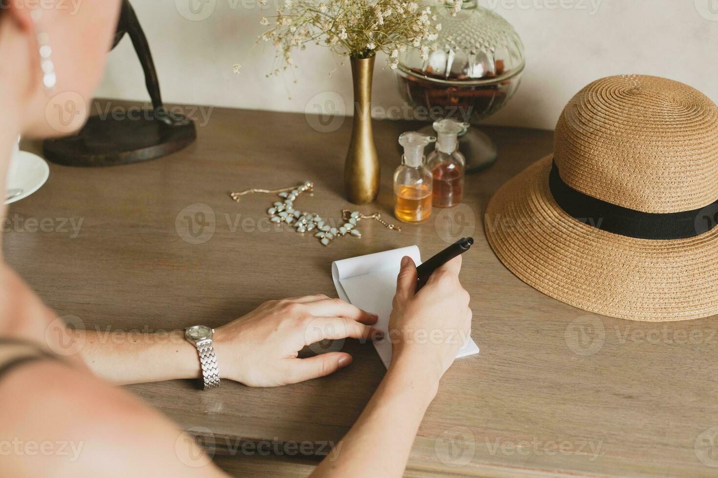 jong elegant mooi vrouw zittend Bij tafel in toevlucht hotel kamer, schrijven een brief, Holding pen foto