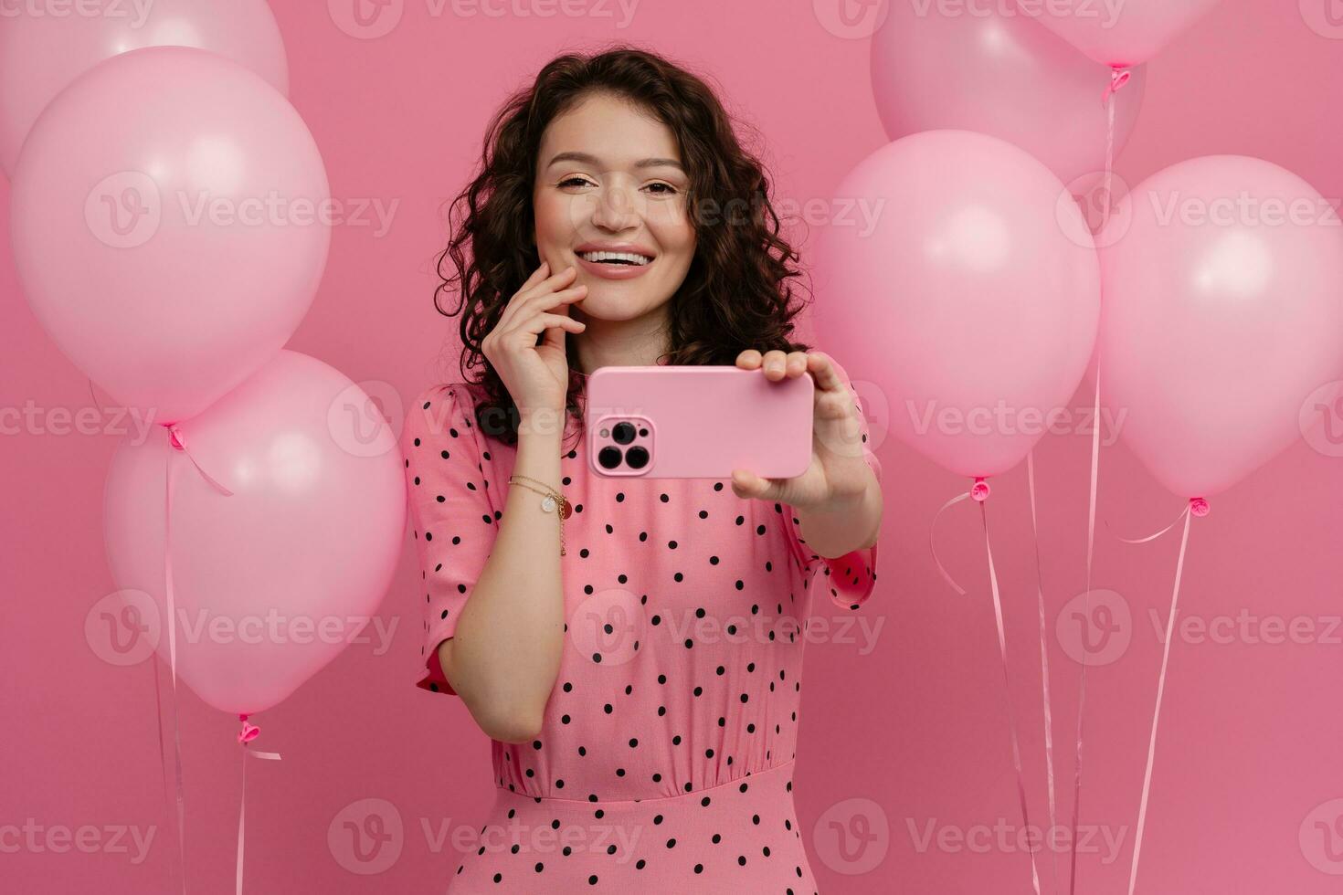 mooi jong vrouw poseren geïsoleerd Aan roze studio achtergrond met roze lucht baloons en smartphone foto