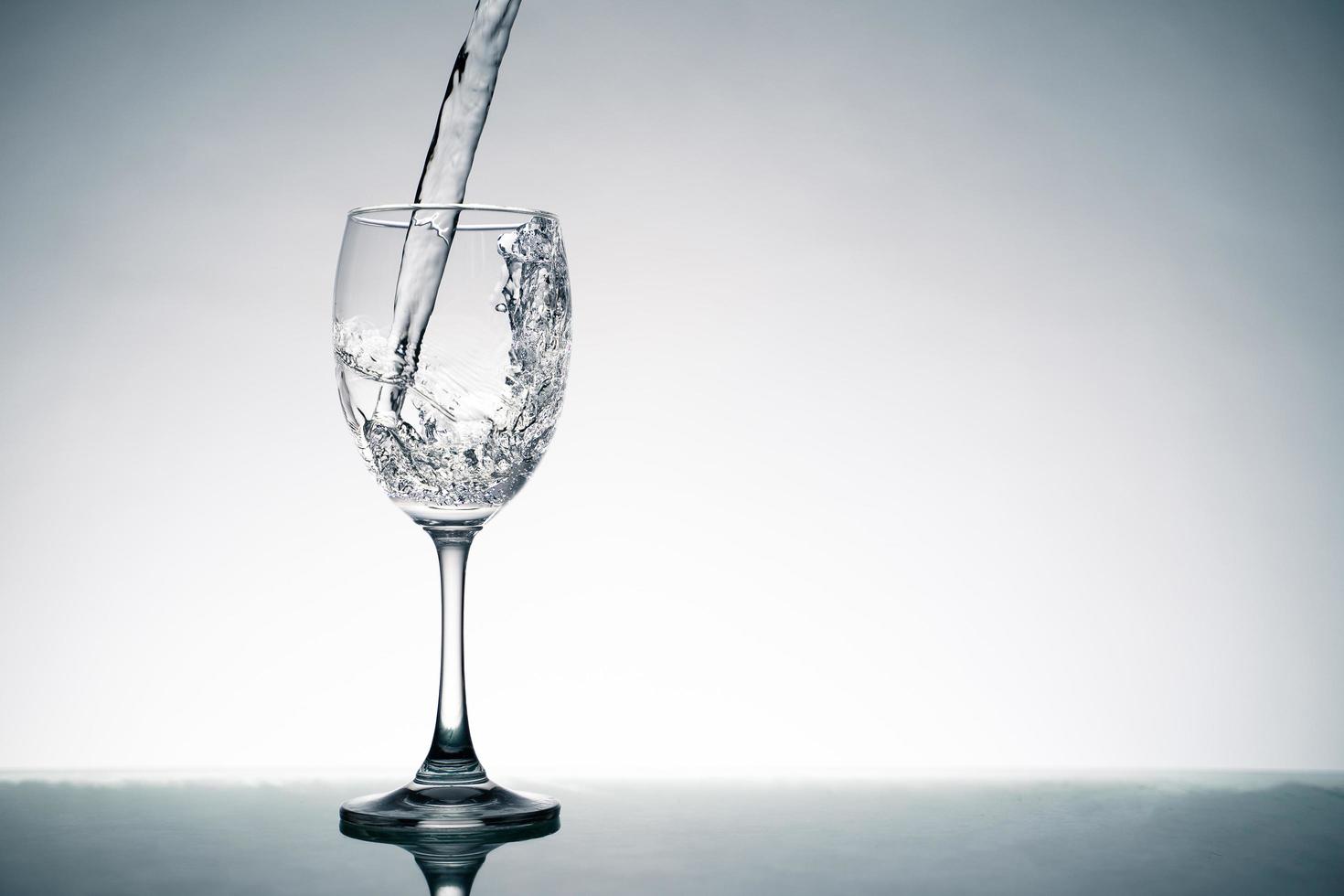 close-up van plons kristalhelder water dat in het wijnglas op tafel stroomt. foto