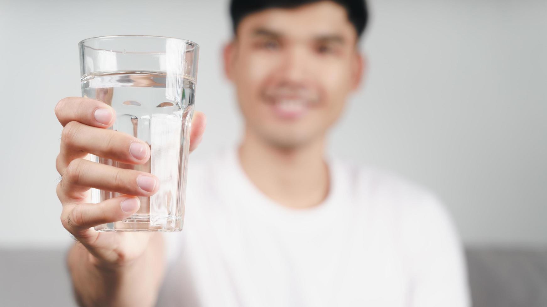 knappe aziatische man die een glas water drinkt op de bank in de woonkamer foto