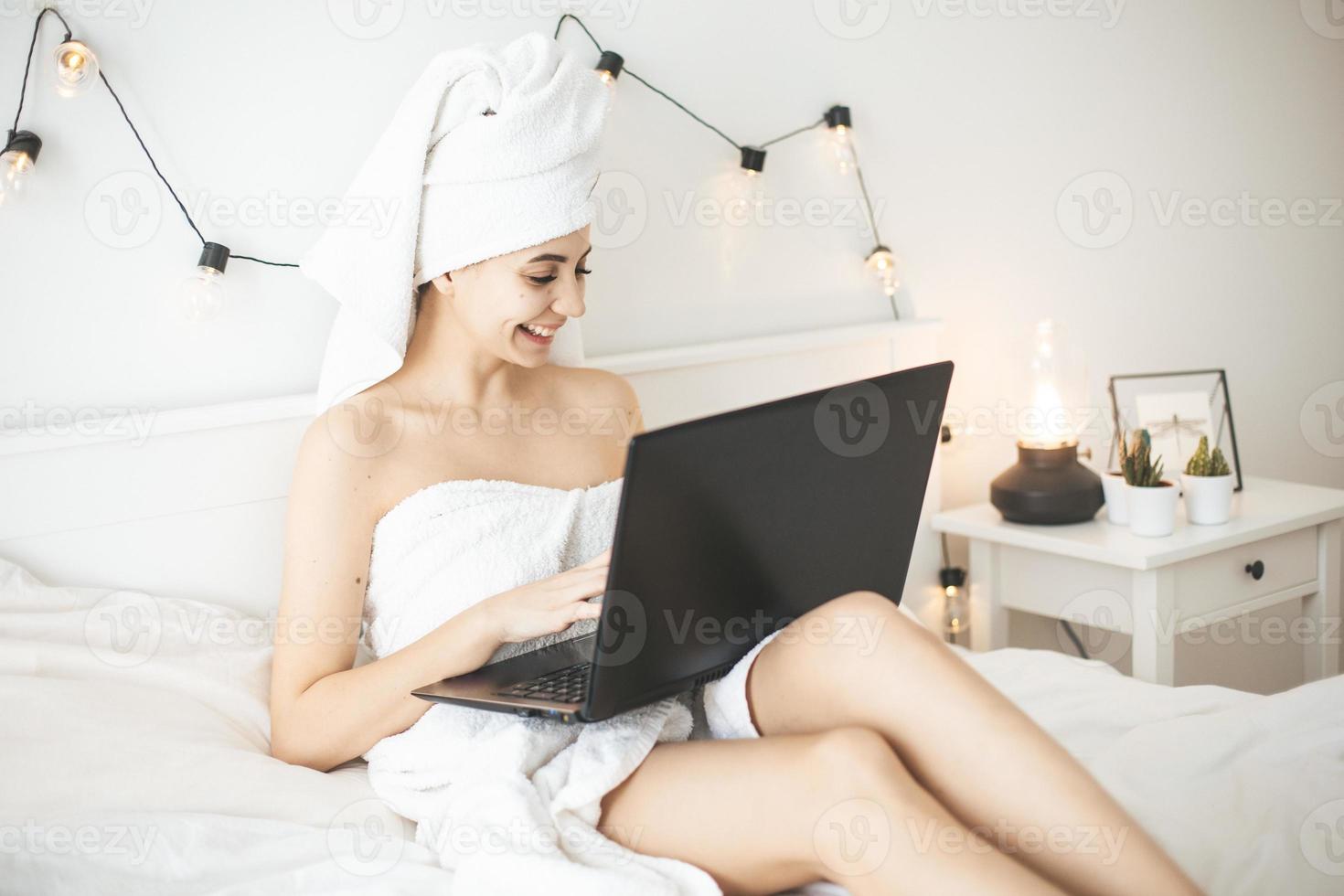 jonge vrouw die in wit bed werkt die laptop met behulp van. foto