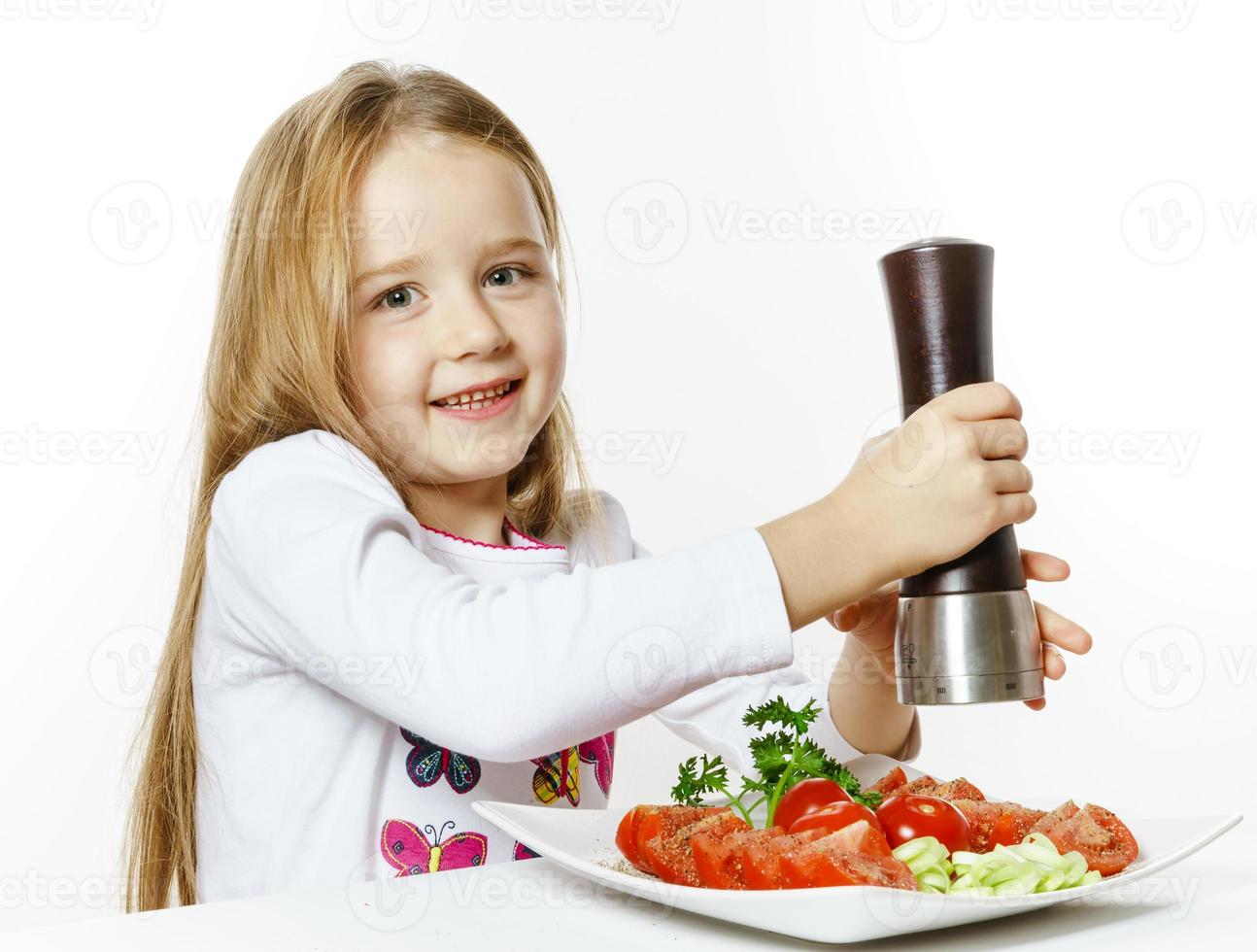 schattig klein meisje met salade en peperdoos foto