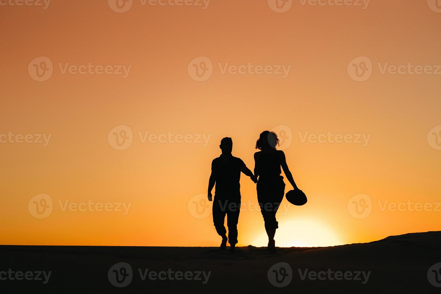 silhouetten van een gelukkig jong koppel op een achtergrond van oranje zonsondergang in de zandwoestijn foto