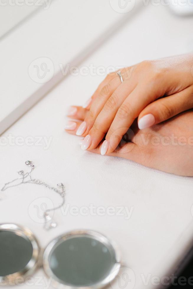bruid kruiste zachtjes haar handen op een tafel bij een ronde spiegel foto