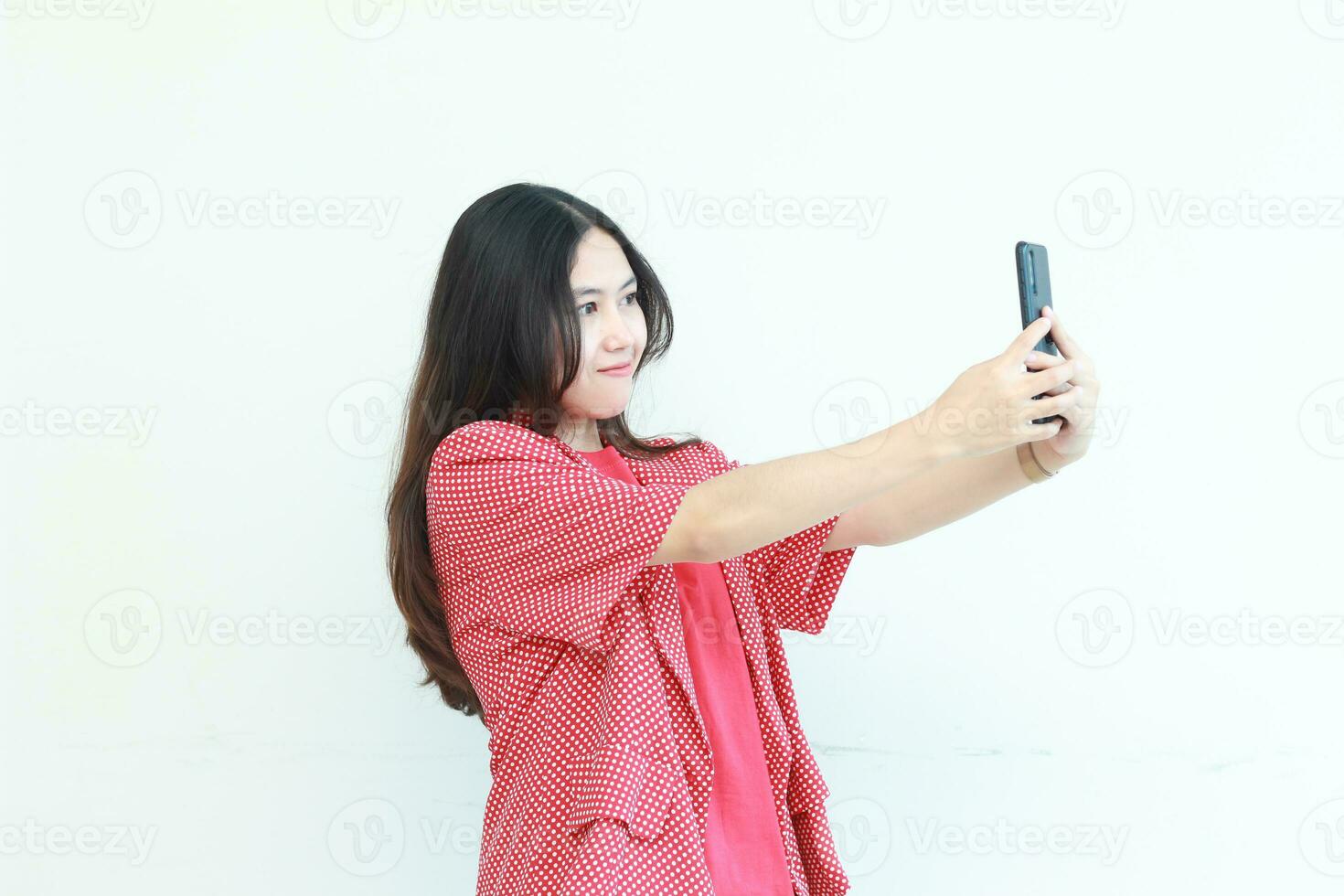portret van mooi Aziatisch vrouw vervelend rood kleding op zoek Bij mobiel telefoon met gelukkig uitdrukking foto