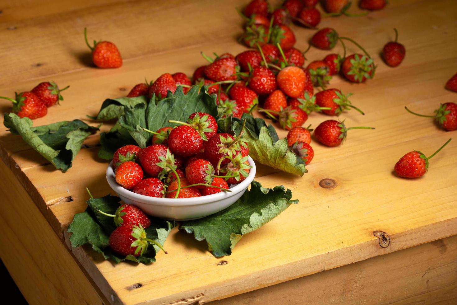 verse aardbeien in een witte keramische kom op een houten tafel op een zwarte achtergrond foto