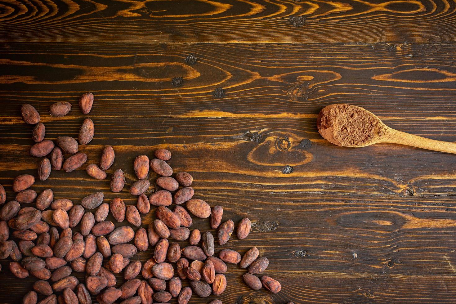 cacaobonen en cacaopoeder in houten lepel op oude natuurlijke houten achtergrond foto