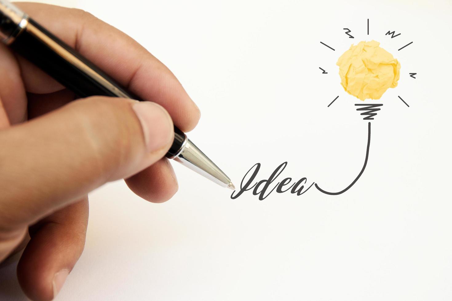 creativiteit inspiratie, ideeën en innovatieconcepten met gloeilamp en papier verfrommeld bal. hand van zakenman schrijven tekst idee met pen. foto