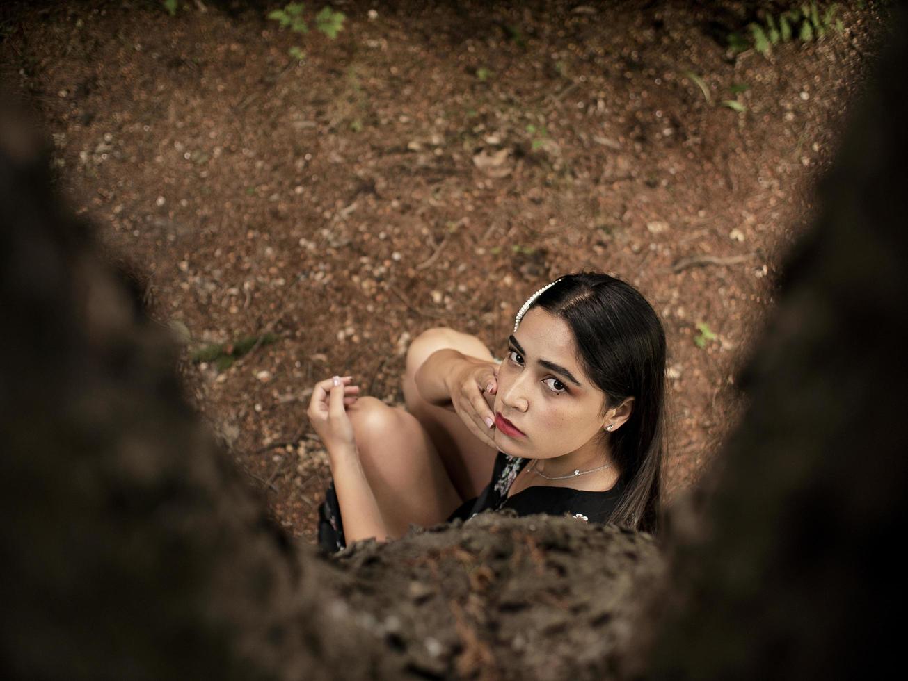aantrekkelijk meisje met een kaukasisch uiterlijk, zittend in de buurt van een boom, met een hand in de buurt van het gezicht. uitzicht van boven foto