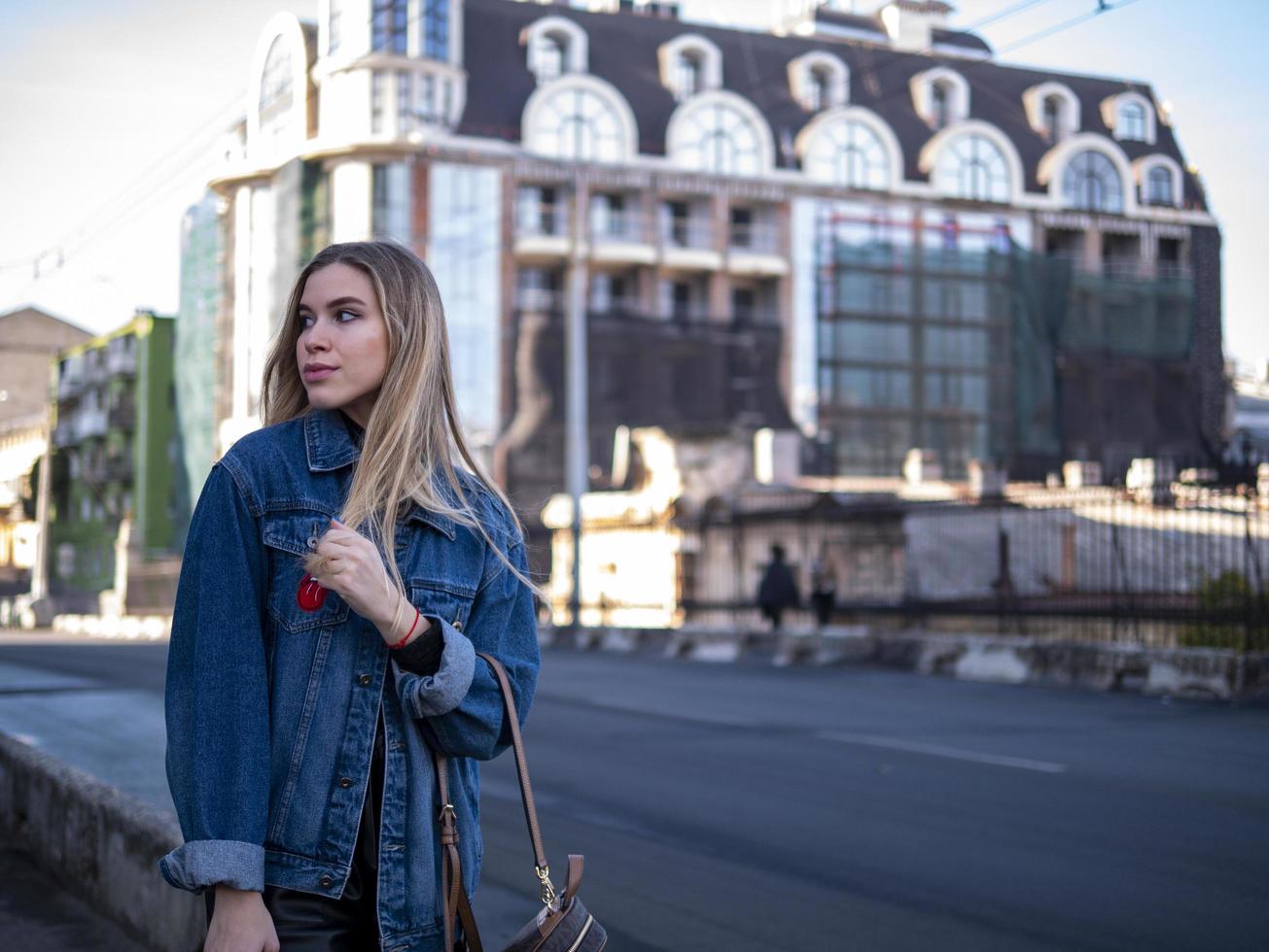 schattige blonde tiener met golvend haar in een spijkerjasje op de brug buiten foto