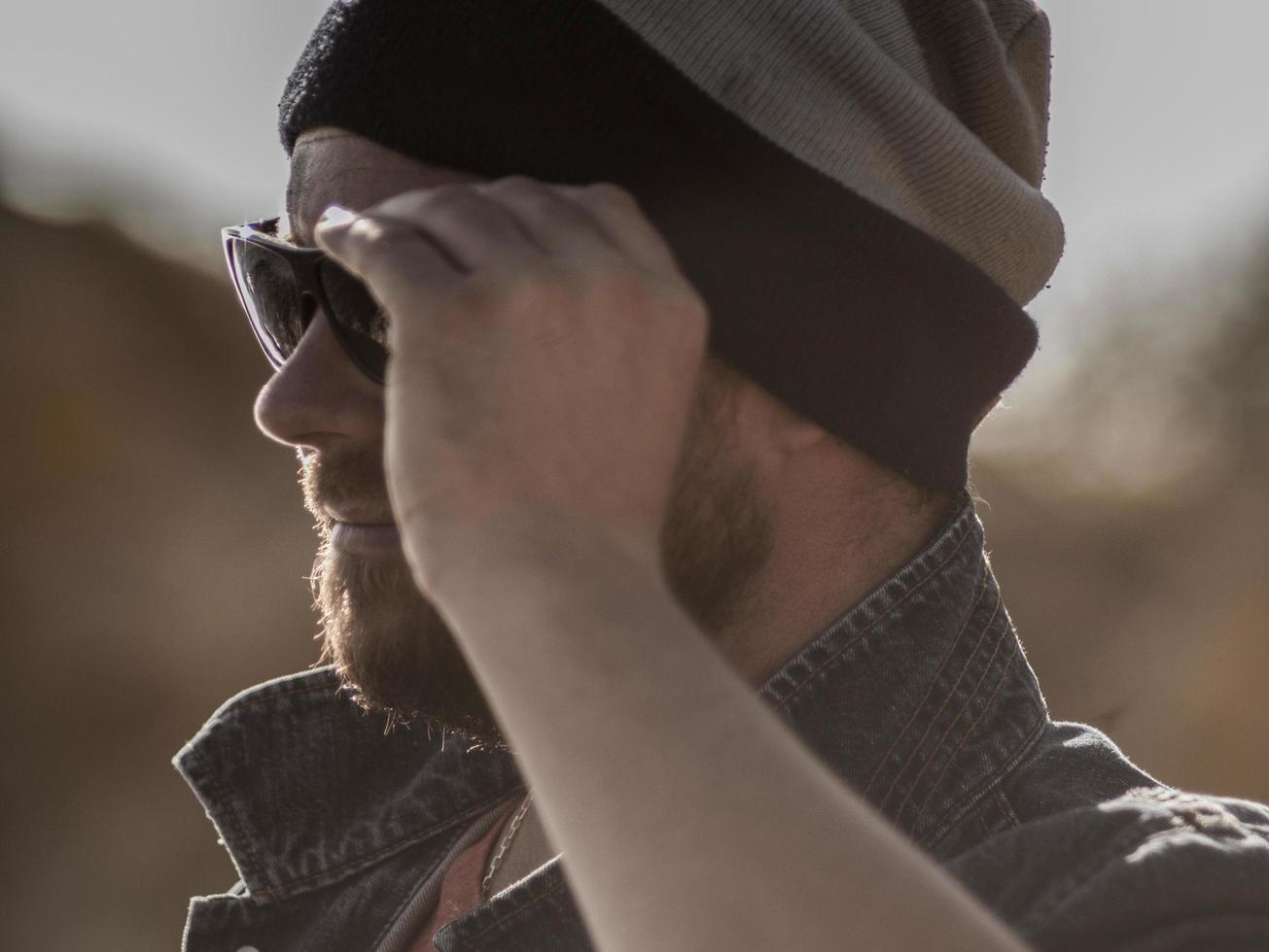 portret van een stijlvolle man met een baard in een gebreide muts en zonnebril foto