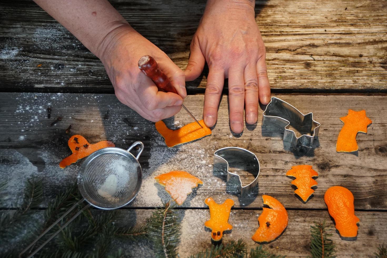 vrouw handen en kerst decoratieve figuren gemaakt van sinaasappelschil op de oude houten tafel. foto