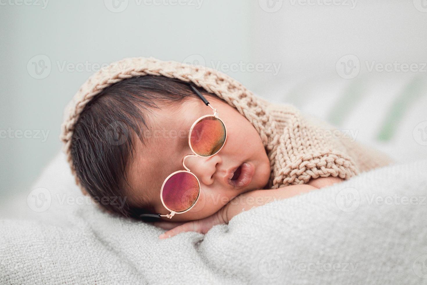 schattige pasgeboren baby rustig slapen op een witte deken. hij draagt een zonnebril foto