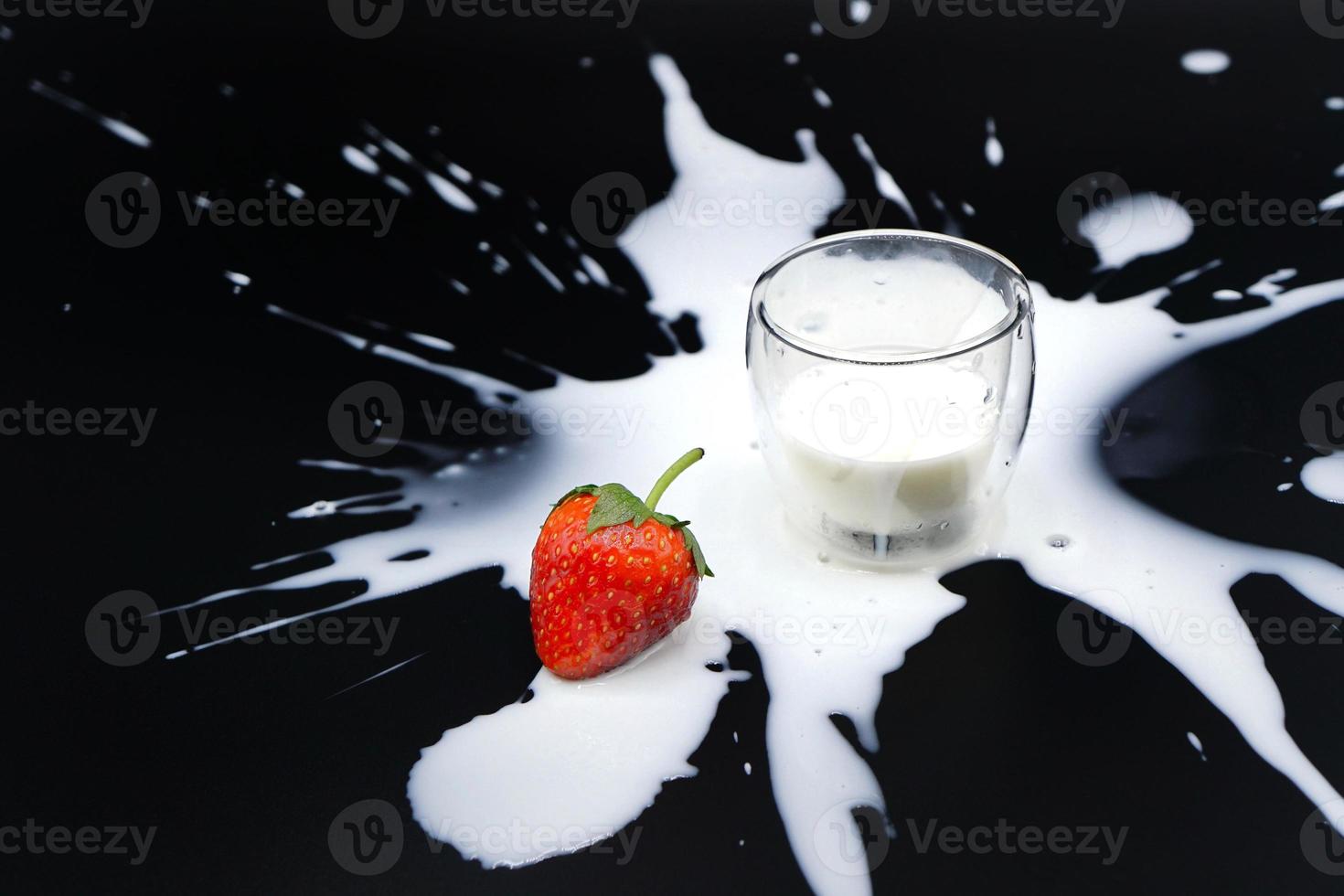 een verse aardbei met een glas melk die buiten het glas op de zwarte achtergrond spettert foto