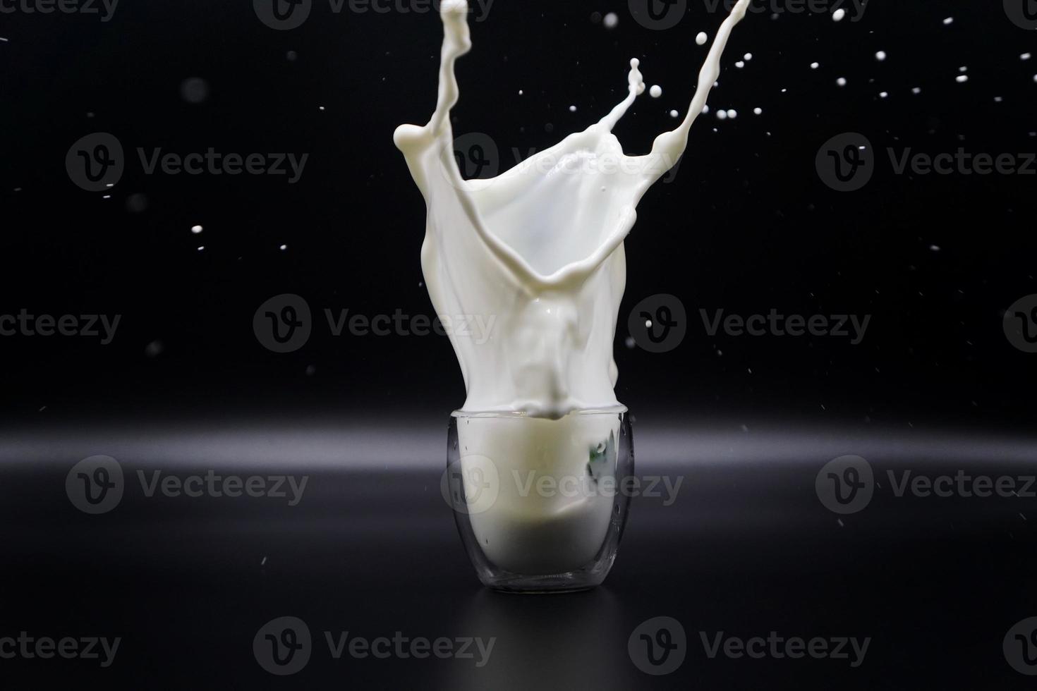 een aardbei die in een glas melk viel, veroorzaakte melkspatten op de zwarte achtergrond foto