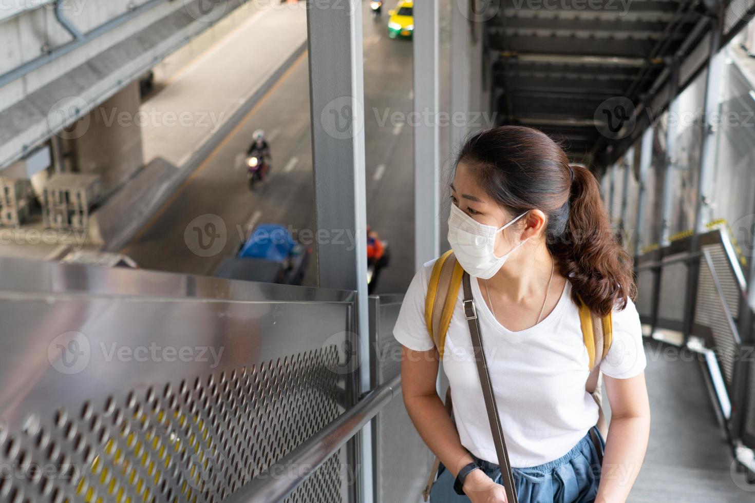 jonge aziatische vrouw met een lachend gezicht en het dragen van gezichtsmaskers als richtlijn voor sociale afstand. ze gebruikt de roltrap om naar boven te gaan naar het luchttreinstation. nieuwe normale levensstijl, covid-19, coronavirusconcept foto