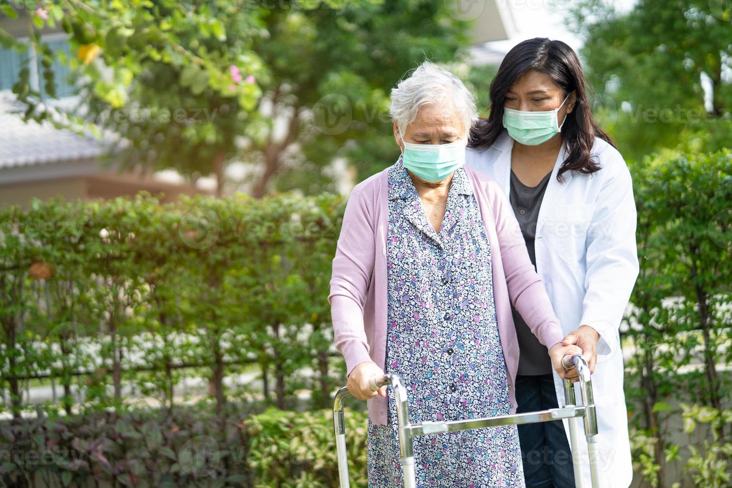 arts helpt aziatische senior of oudere oude dame vrouw lopen met rollator en het dragen van een gezichtsmasker ter bescherming van de veiligheidsinfectie en het doden van het nieuwe coronavirus covid-19 virus. foto