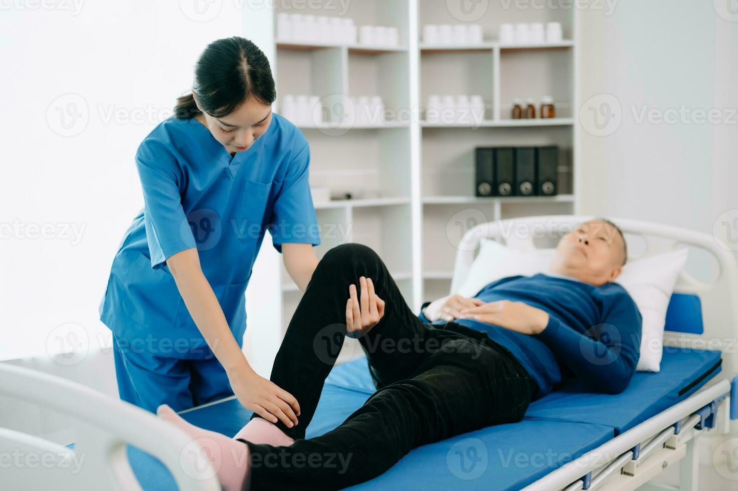 fysiotherapeut helpen geduldig terwijl uitrekken zijn been in bed in kliniek foto