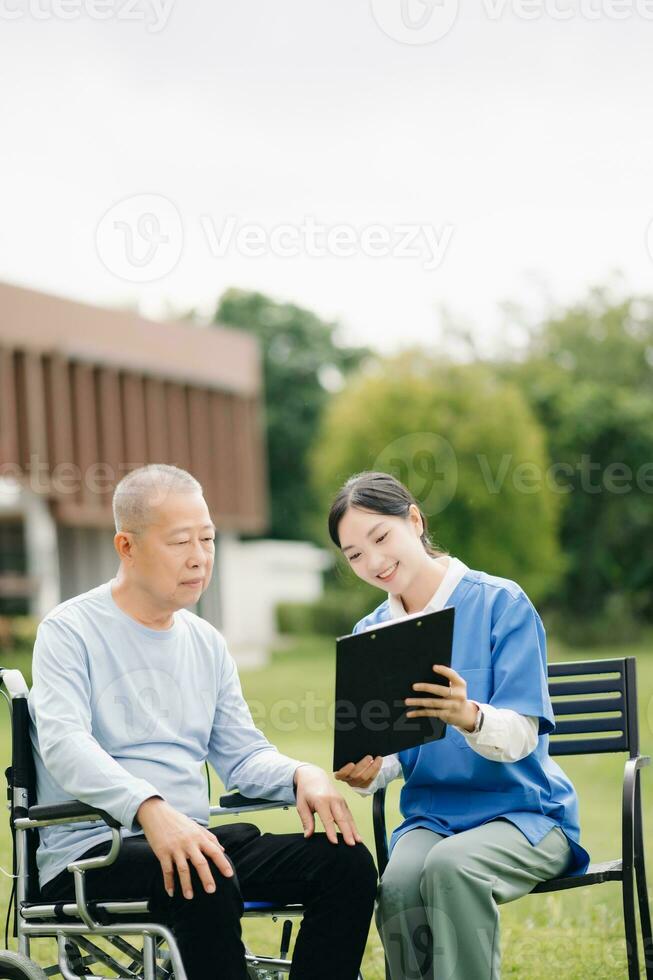 ouderen Aziatisch senior Mens Aan rolstoel met Aziatisch voorzichtig verzorger en aanmoedigen geduldig, wandelen in tuin. met zorg van een verzorger en senior Gezondheid verzekering. foto