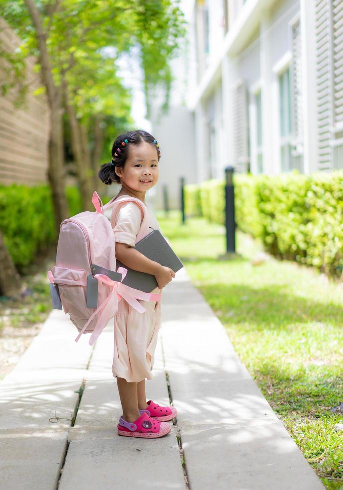 klein meisje met boek en rugzak wandelen in het park klaar terug naar school foto