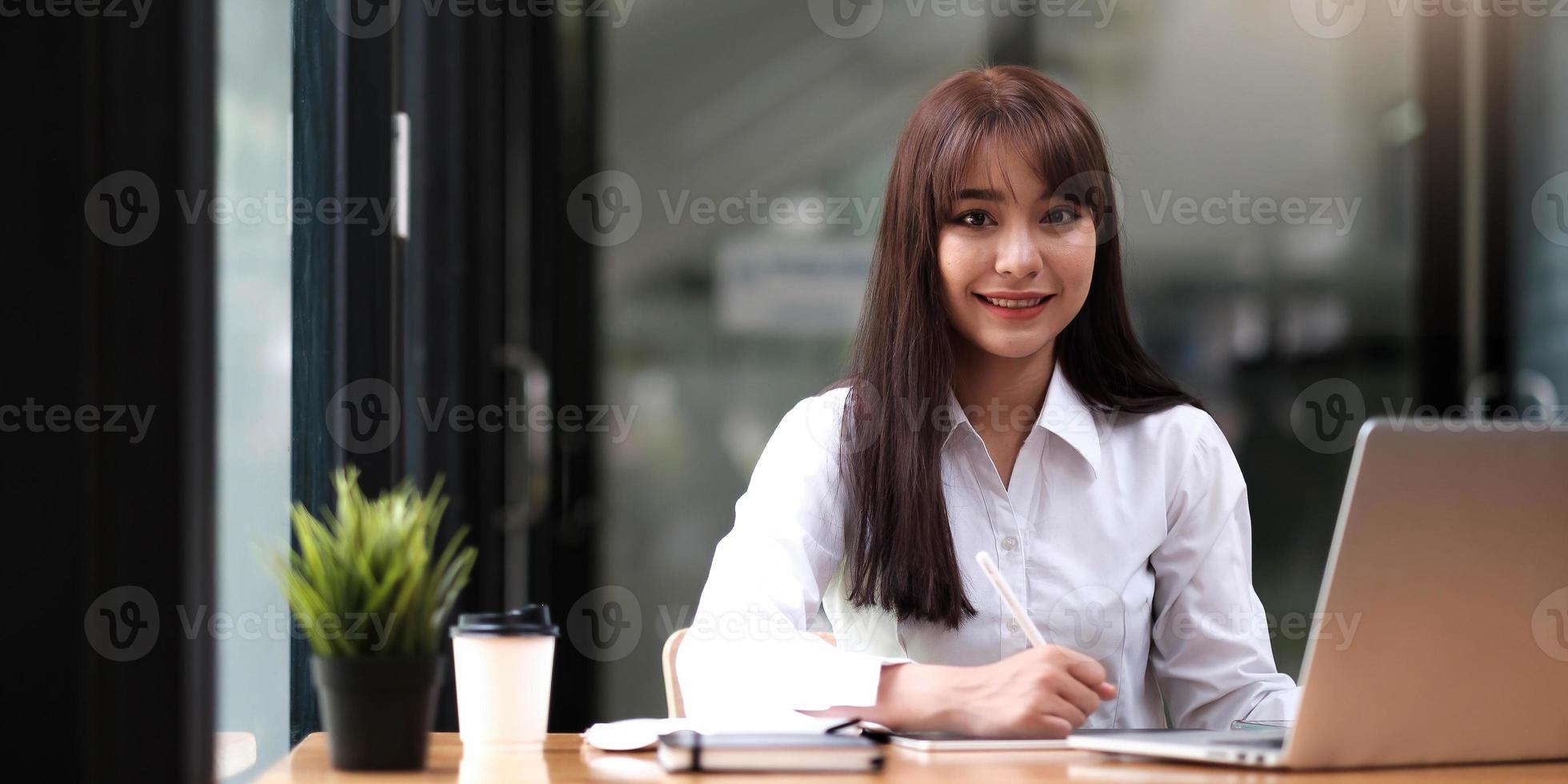 portret van een mooie jonge vrouw die studeert terwijl ze aan tafel zit foto