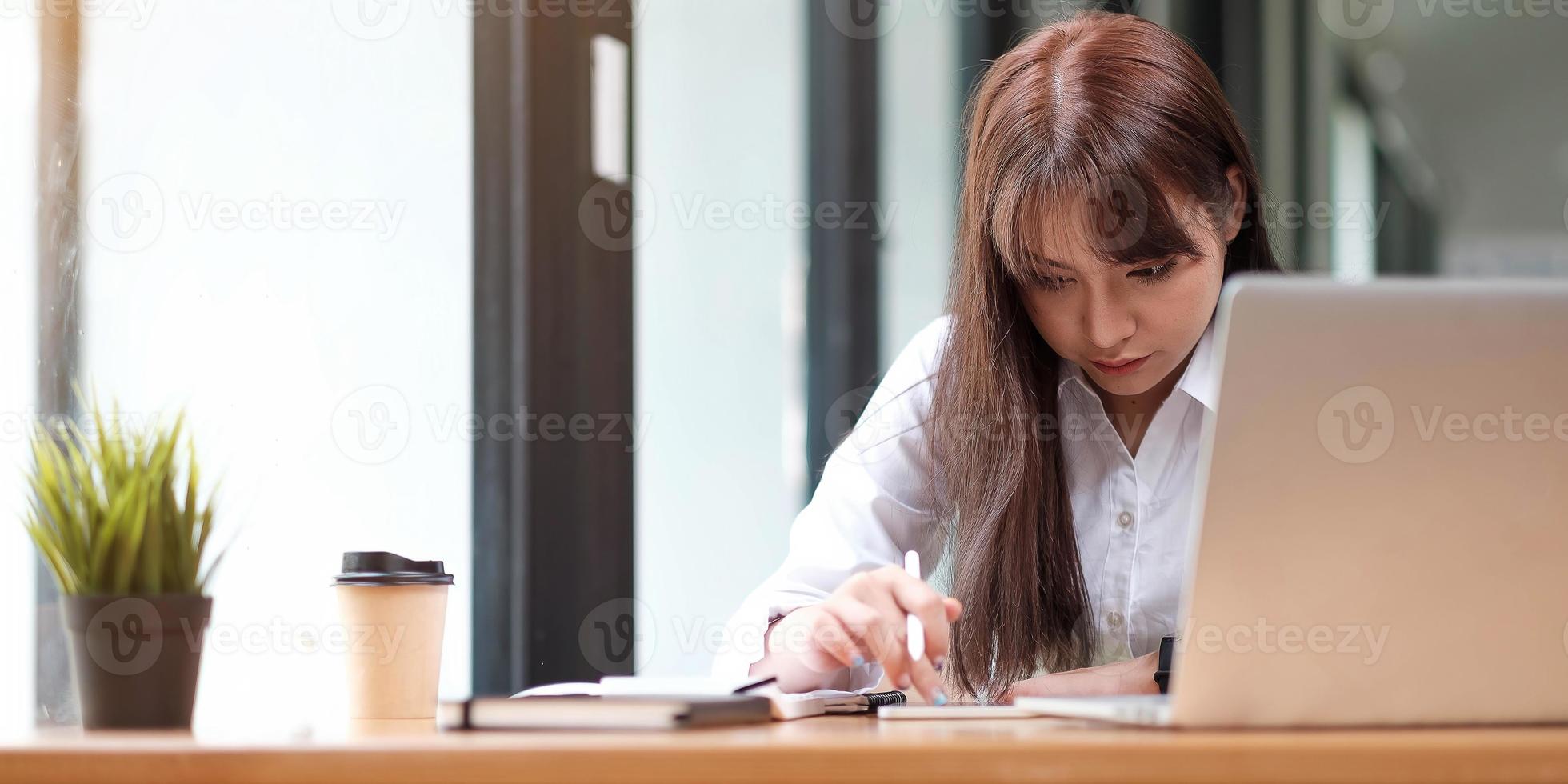 portret van een mooie jonge vrouw die studeert terwijl ze aan tafel zit foto