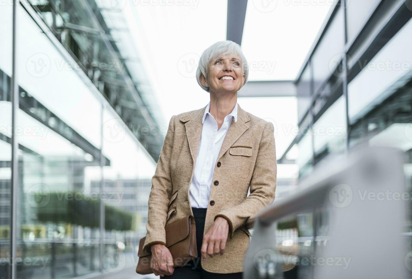 glimlachen senior zakenvrouw leunend Aan traliewerk in de stad op zoek omhoog foto