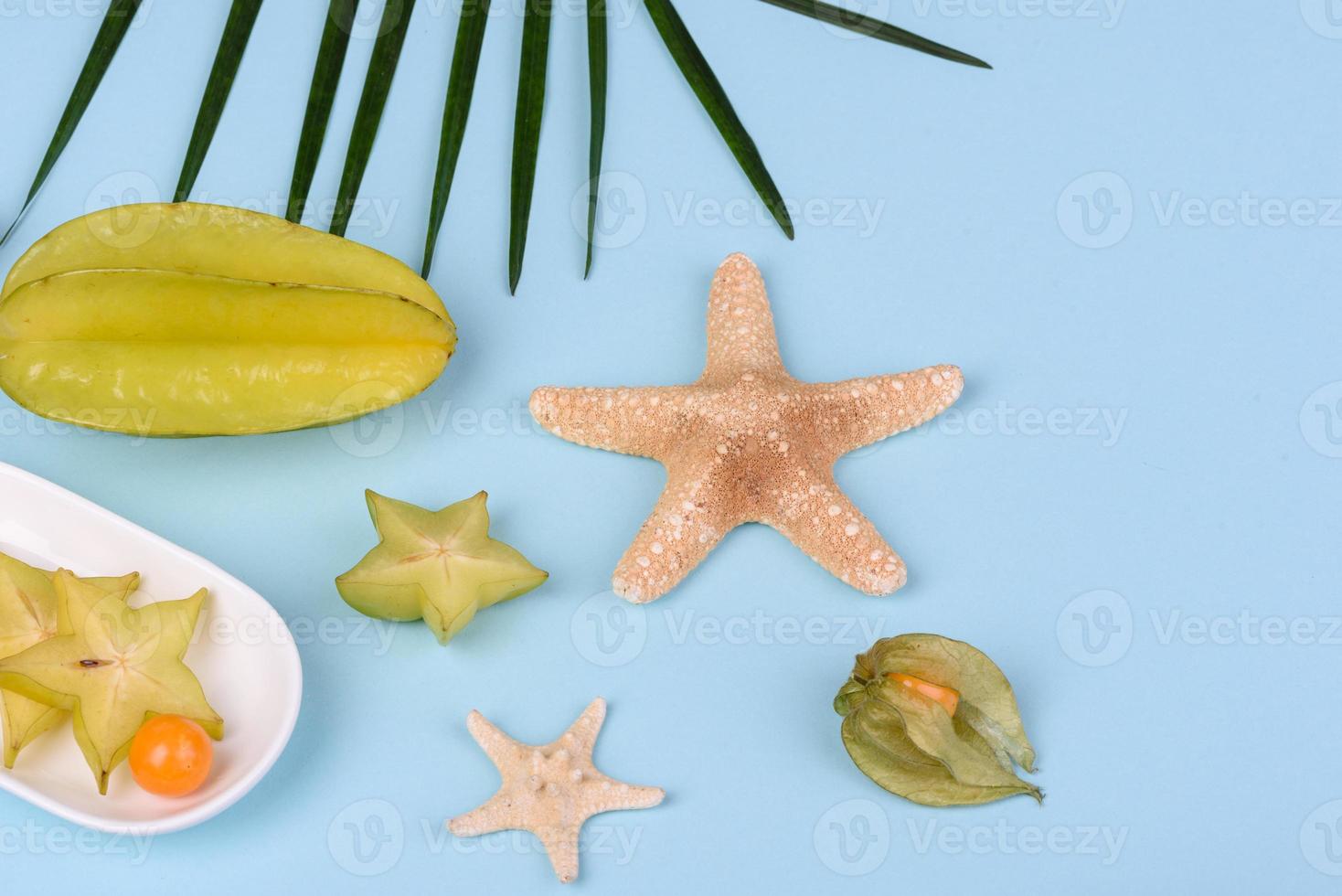 fruitcarambol, strandaccessoires en gebladerte van een tropische plant op gekleurd papier foto