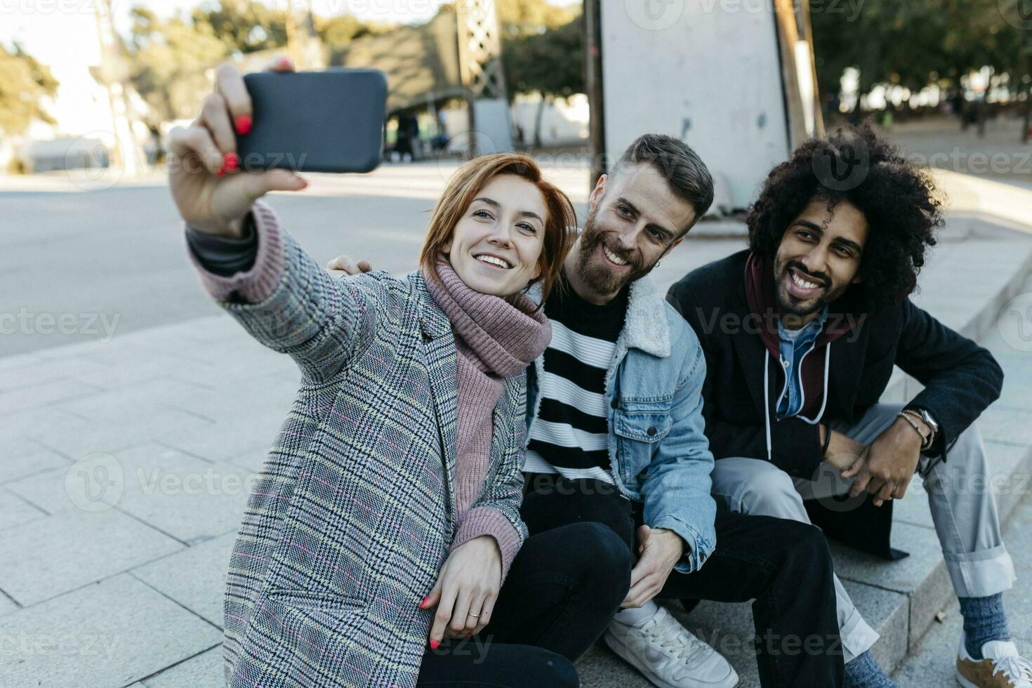 drie gelukkig vrienden zittend buitenshuis nemen een selfie foto