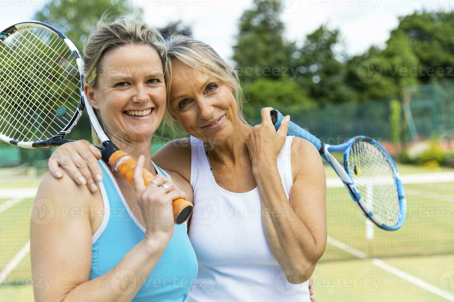 portret van twee gelukkig volwassen Dames Aan gras rechtbank Bij tennis club foto