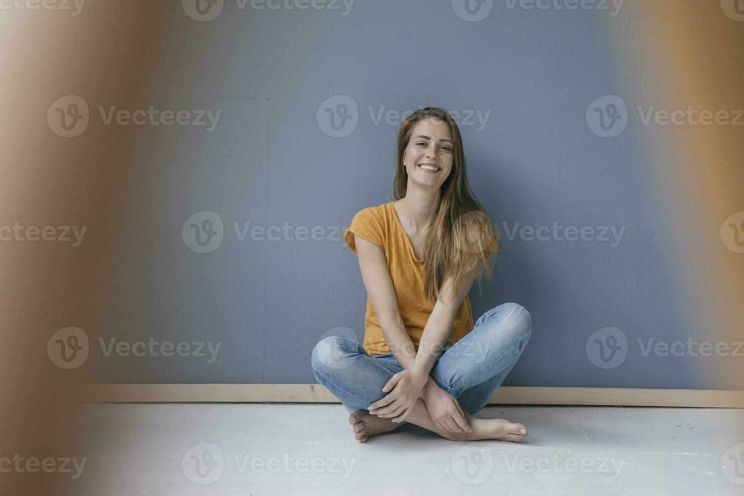 gelukkig vrouw zittend Aan grond, blootsvoets met poten gekruist, lachend foto