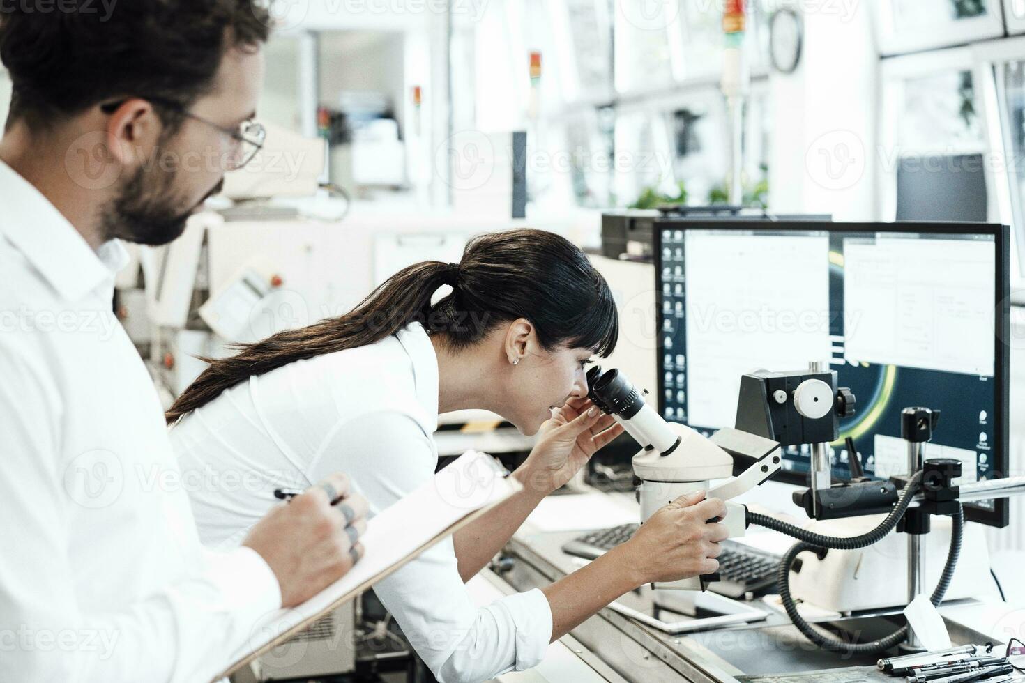 vrouw bedrijf professioneel op zoek door microscoop terwijl staand door mannetje collega Bij laboratorium foto